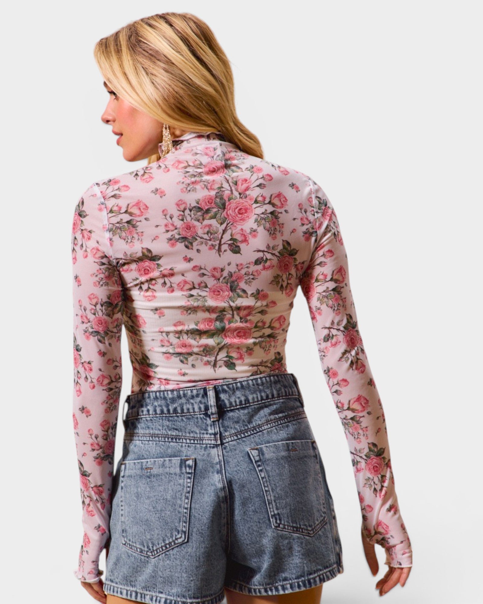 Woman wearing a floral long-sleeve top and denim shorts on a white background