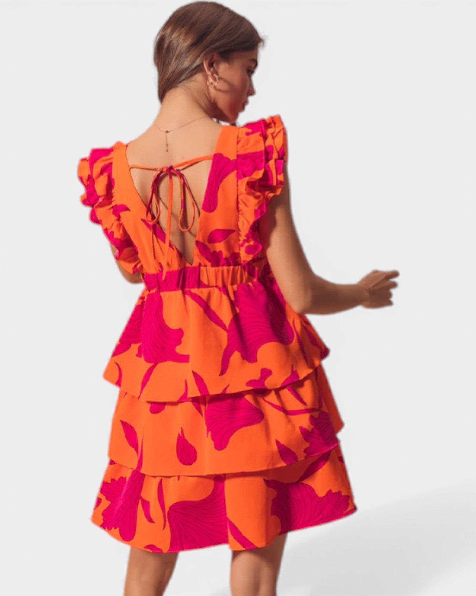Woman wearing a bright orange and pink dress with ruffled layers on a white background