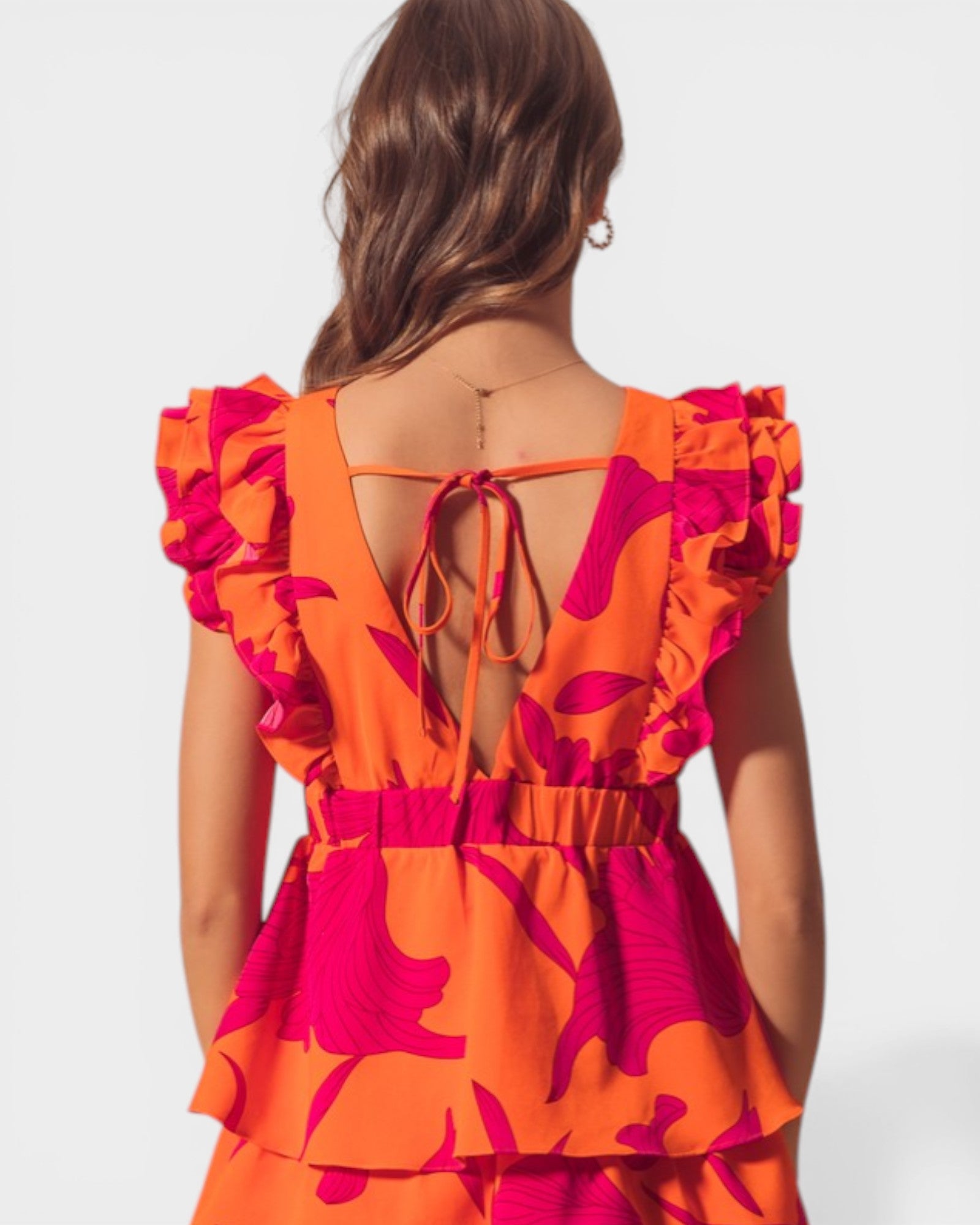 Woman wearing an orange and pink floral dress with a open back on a white background