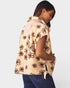 Woman wearing a beige floral-patterned cape over a pink top on a light gray background