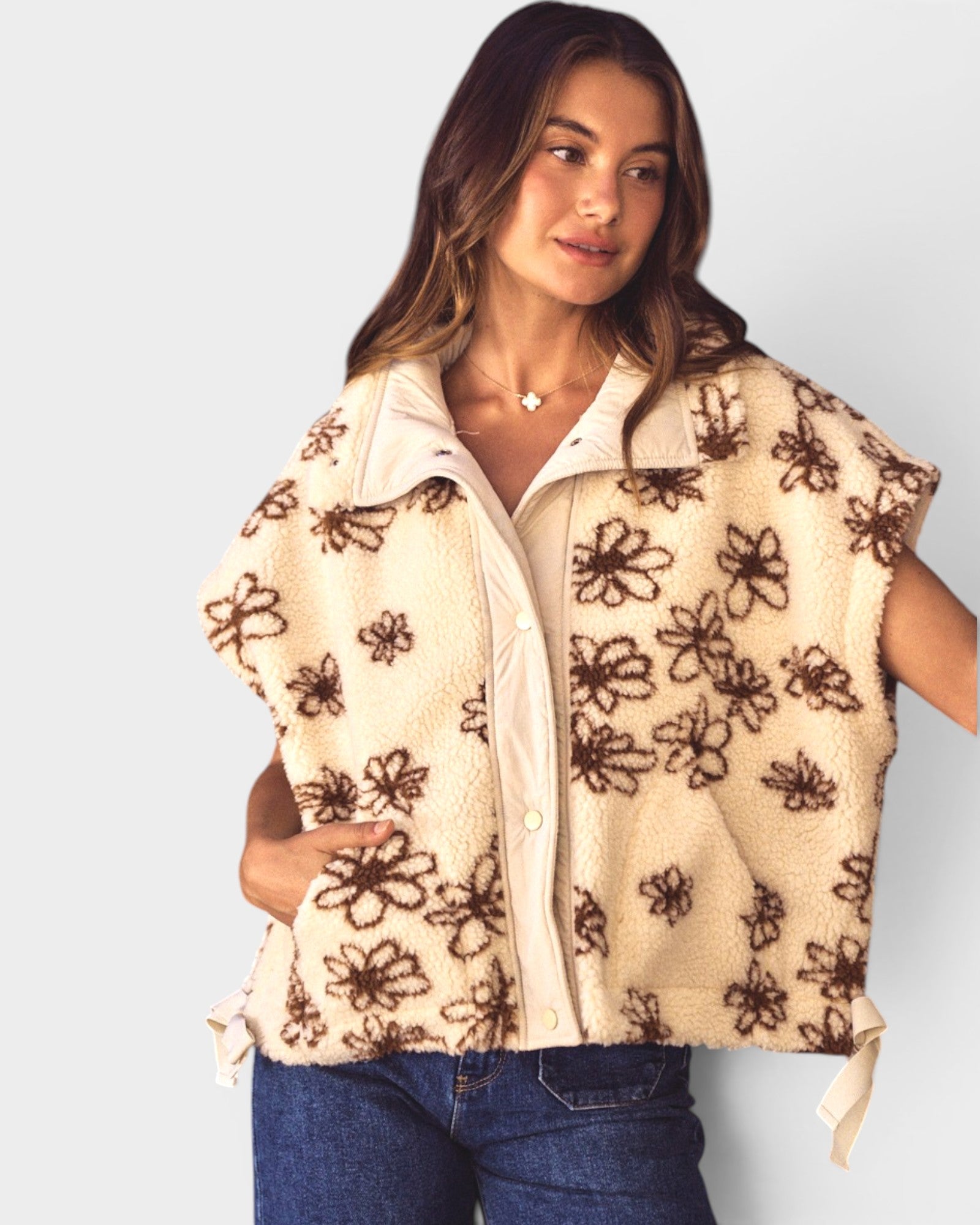 Woman wearing a beige vest with brown floral patterns on a plain background