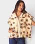 Woman wearing a beige vest with brown floral patterns on a plain background