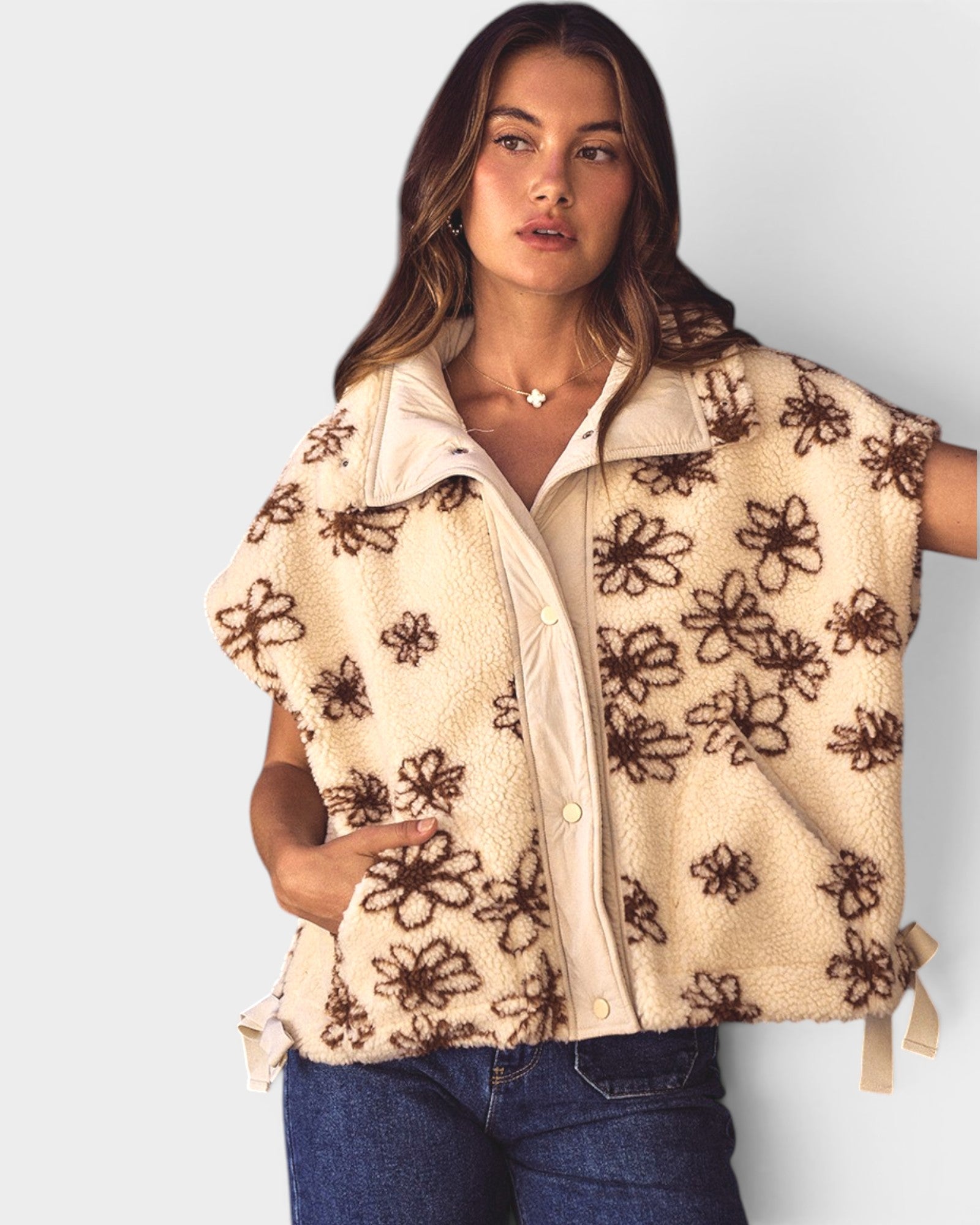 Woman wearing a beige vest with brown floral patterns on a plain background