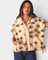 Woman wearing a beige vest with brown floral patterns on a plain background