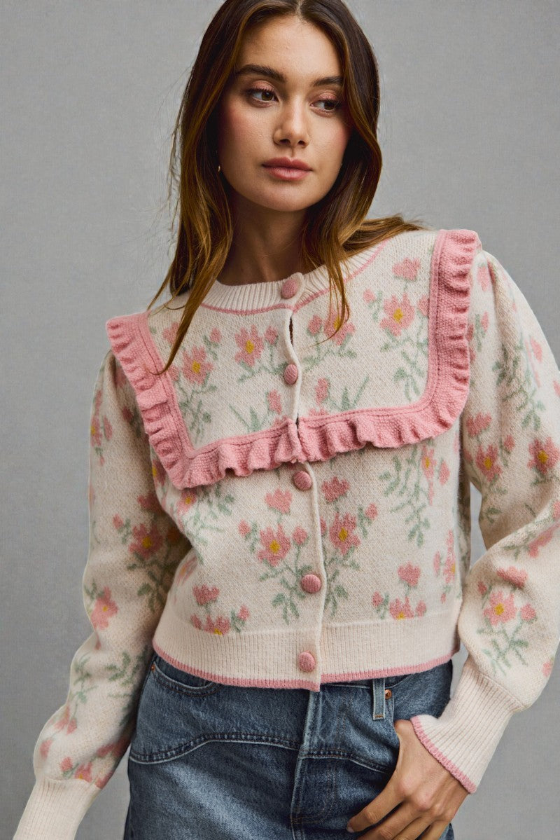 Woman wearing a floral cardigan with pink trim against a gray background
