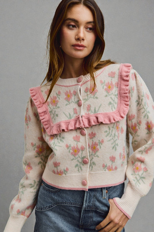 Woman wearing a floral cardigan with pink trim against a gray background