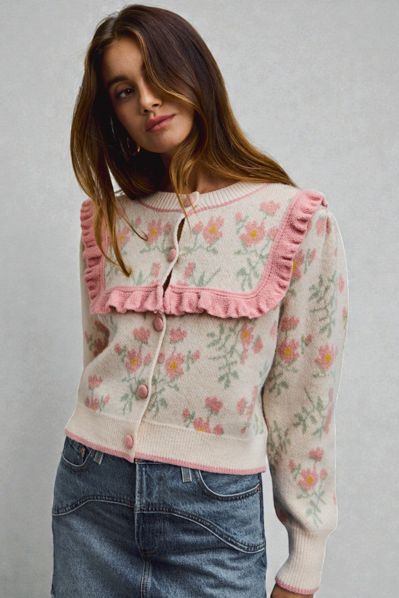 Woman wearing a floral cardigan with pink ruffles on a gray background