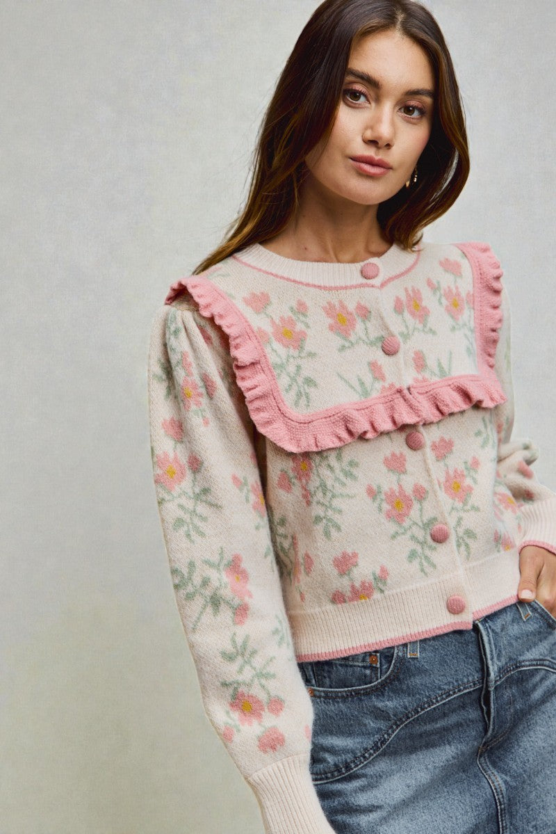 Woman wearing a floral sweater with pink ruffled collar against a neutral background