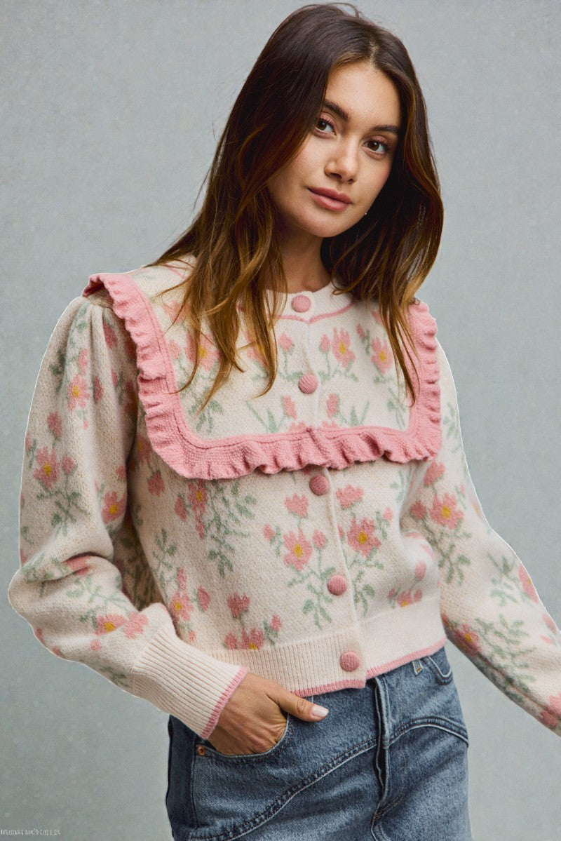 Woman wearing a floral sweater with pink ruffles on a gray background