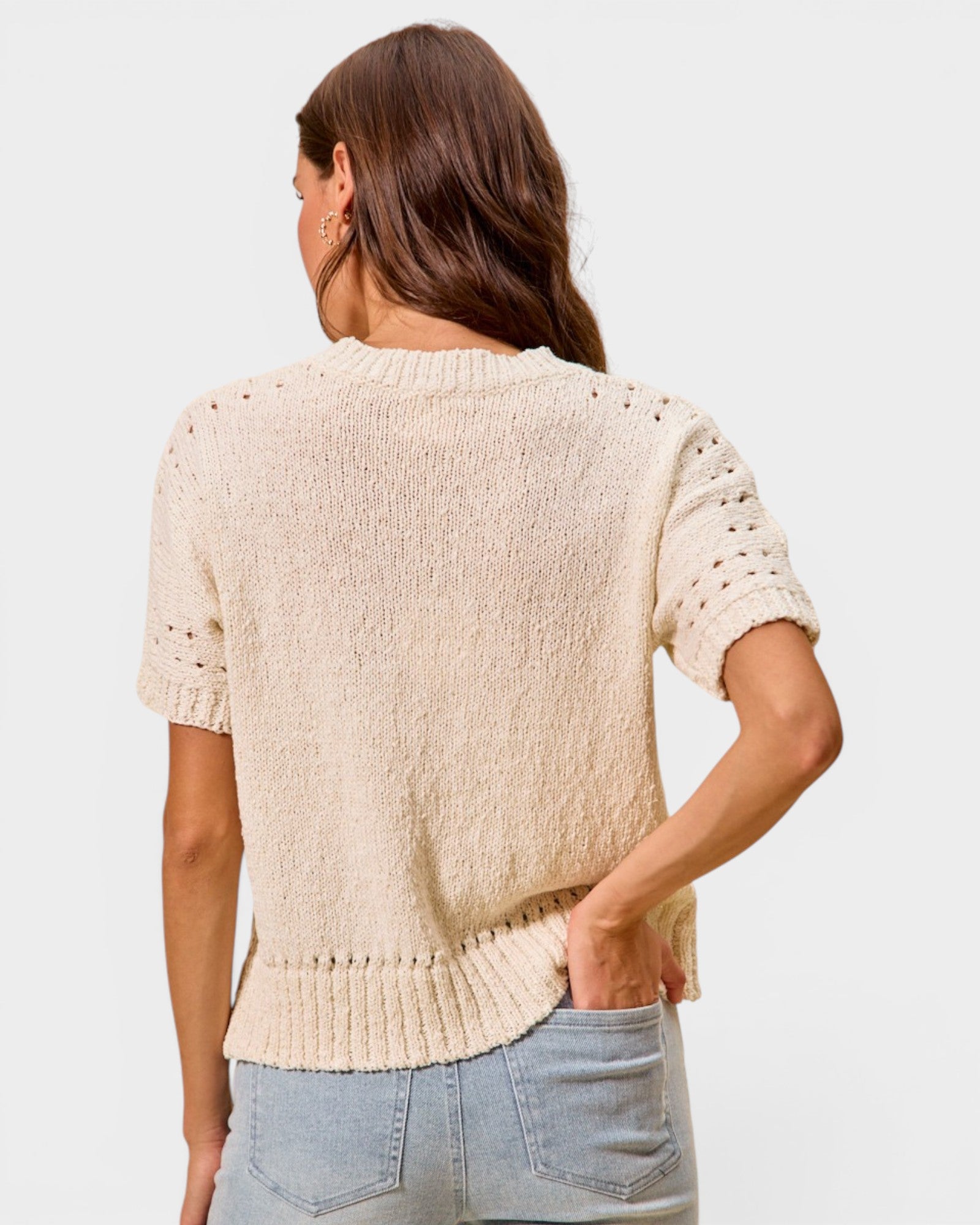 Woman wearing a beige knit sweater and light blue jeans on a plain background