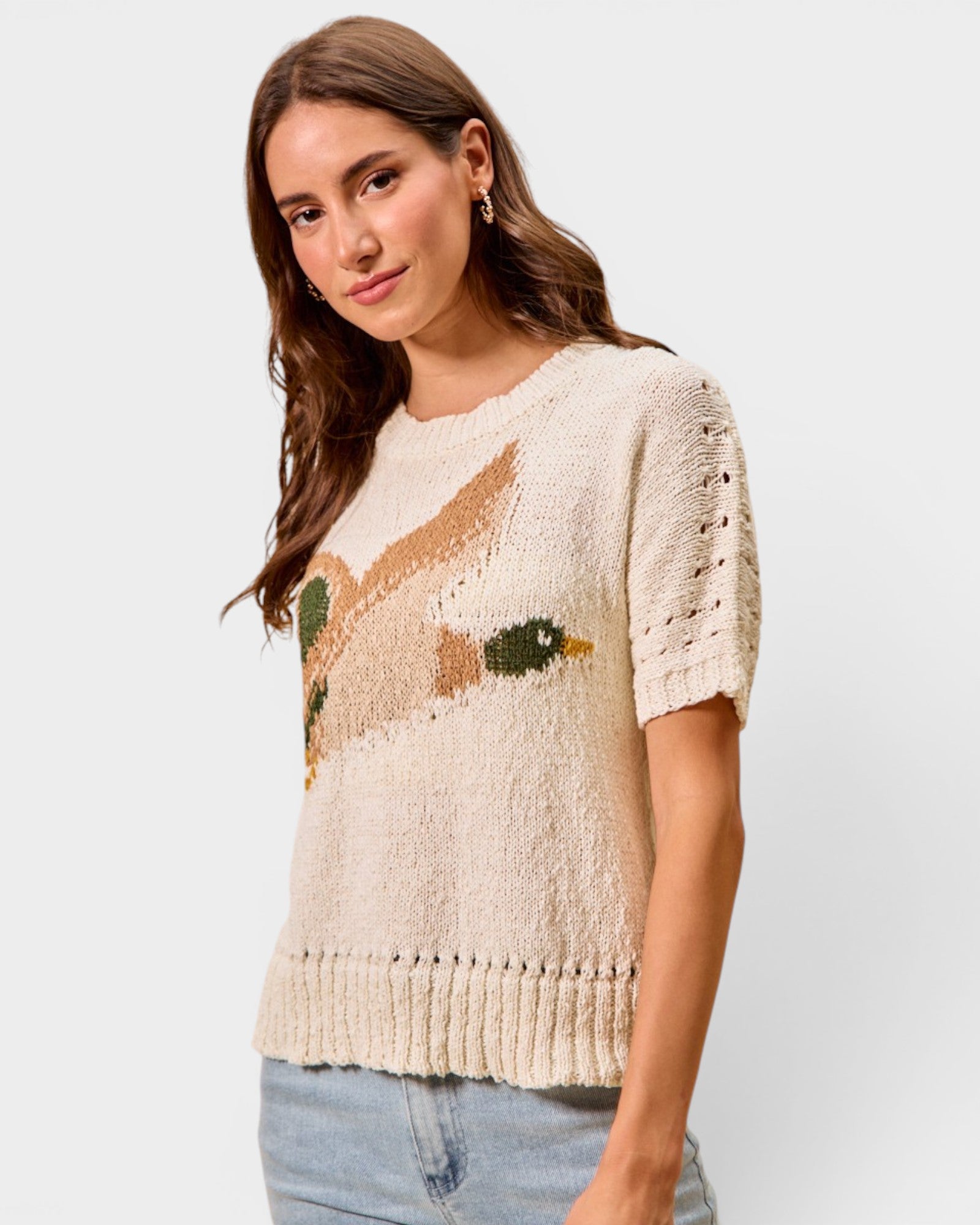 Woman wearing a beige sweater with a fish design on a plain background