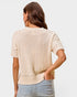 Woman wearing a beige knit sweater and light blue jeans on a plain background