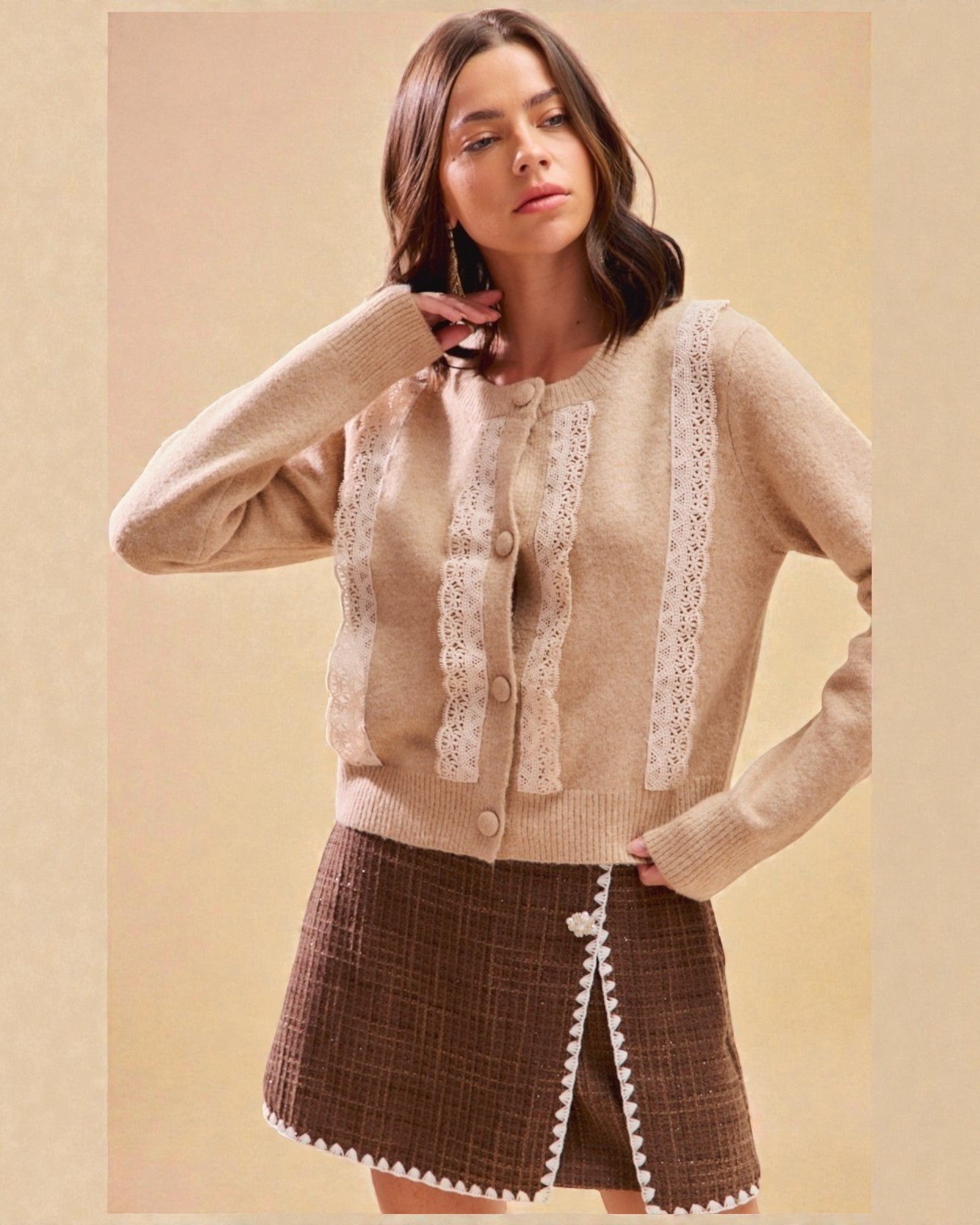Woman wearing a beige cardigan with lace details and a brown skirt on a beige background