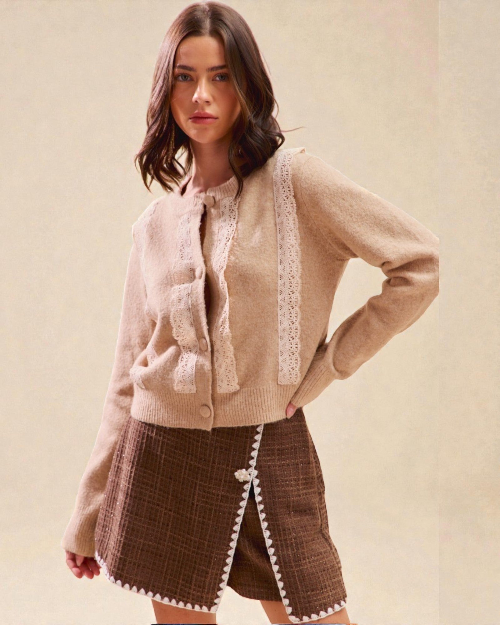 Woman wearing a beige cardigan with lace details and a brown skirt on a beige background