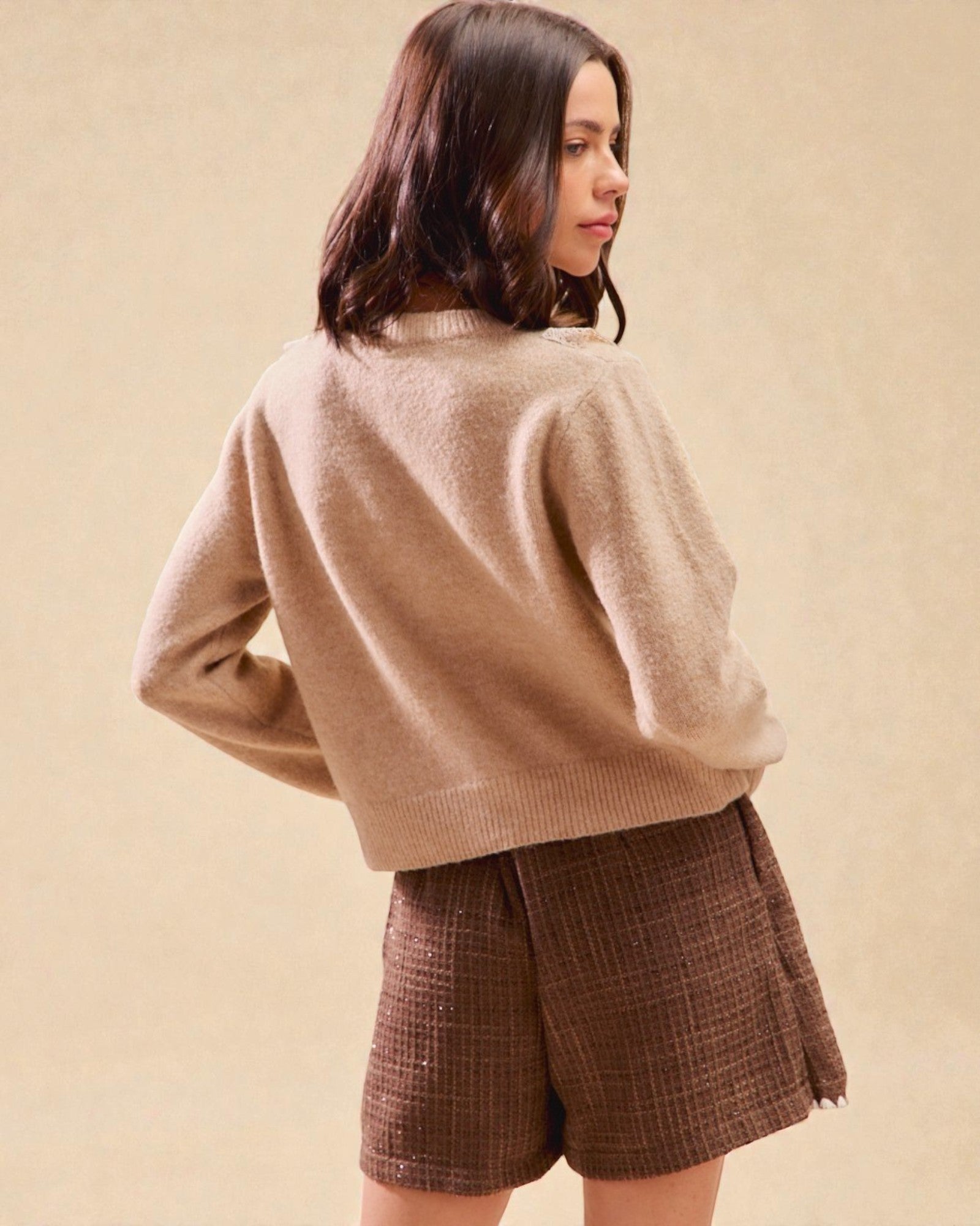 Woman wearing a beige sweater and brown plaid shorts on a beige background