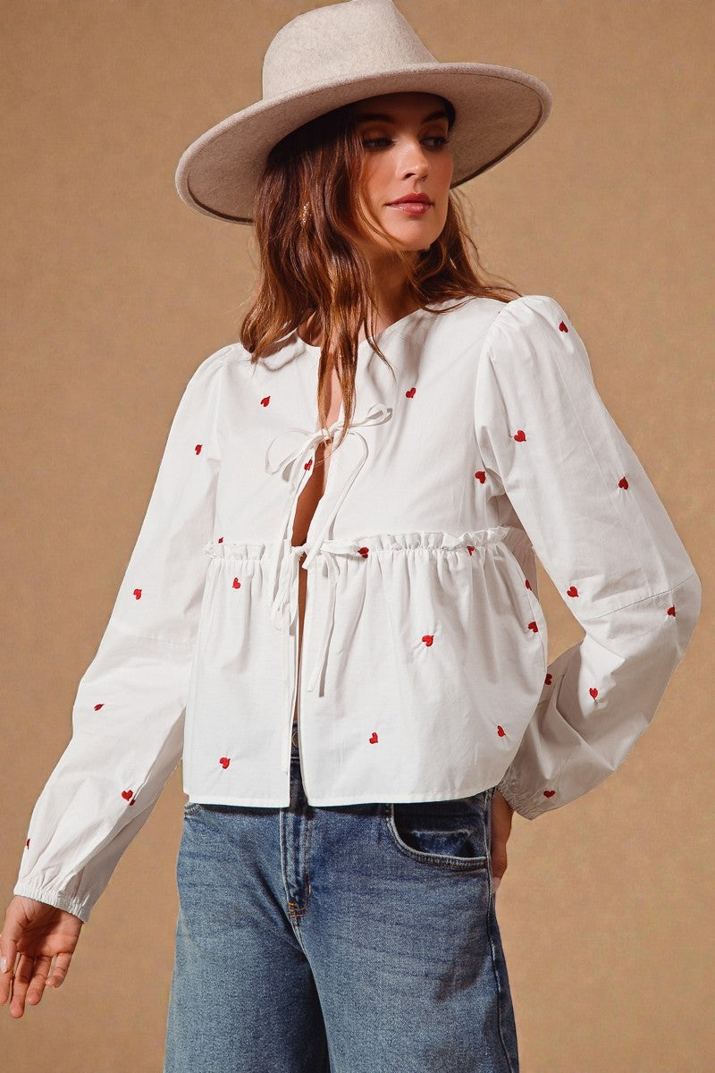 Woman wearing a white blouse with red heart patterns and a beige hat on a beige background