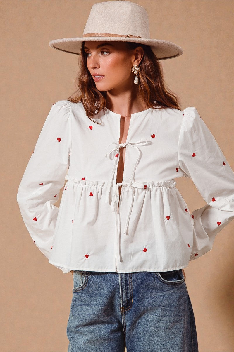 Woman wearing a white blouse with red heart patterns and blue jeans against a beige background