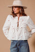 Woman wearing a white blouse with red heart patterns and blue jeans against a beige background