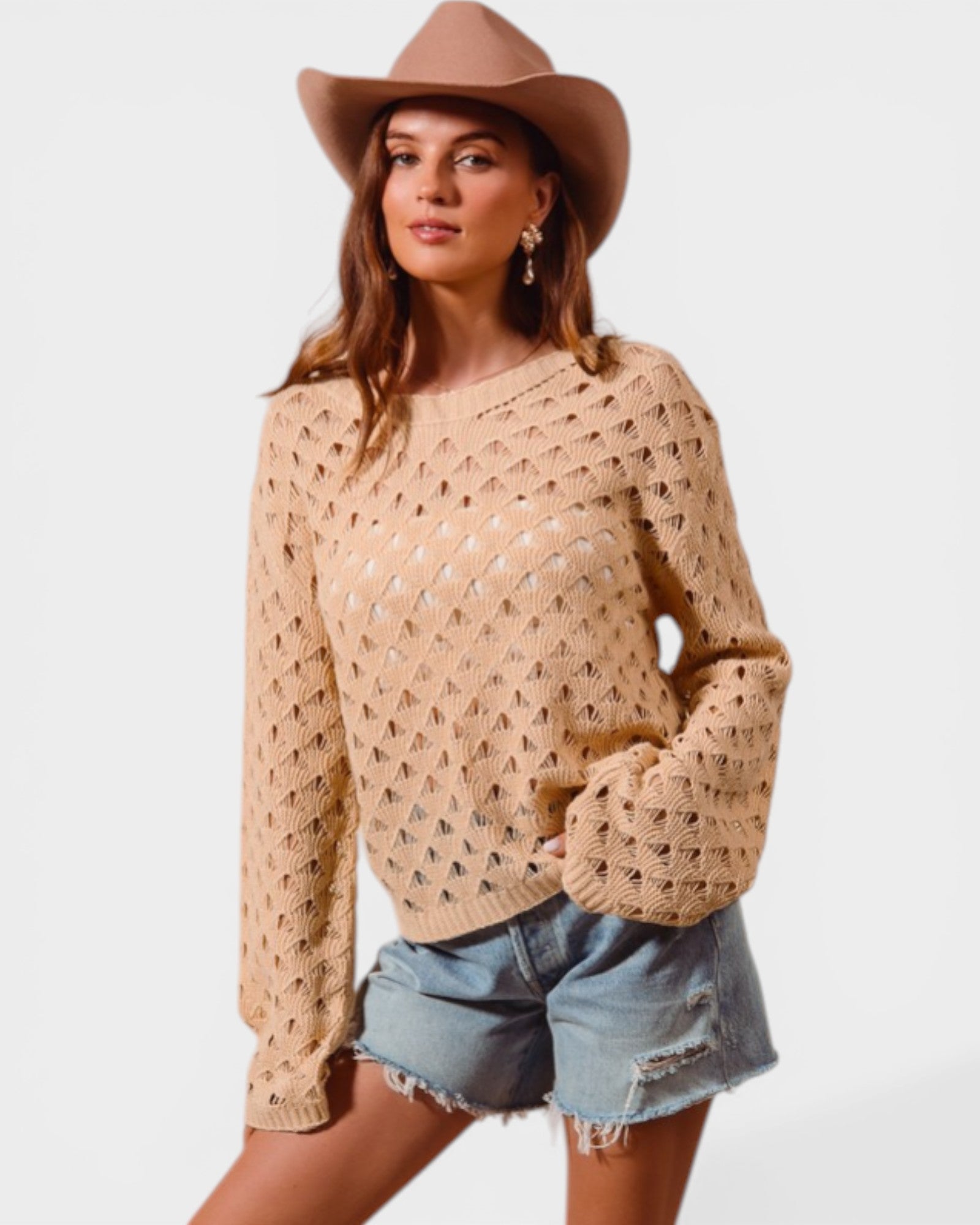 Woman wearing a beige crochet sweater, denim shorts, and a beige hat on a white background