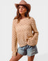 Woman wearing a beige crochet sweater, denim shorts, and a beige hat on a white background