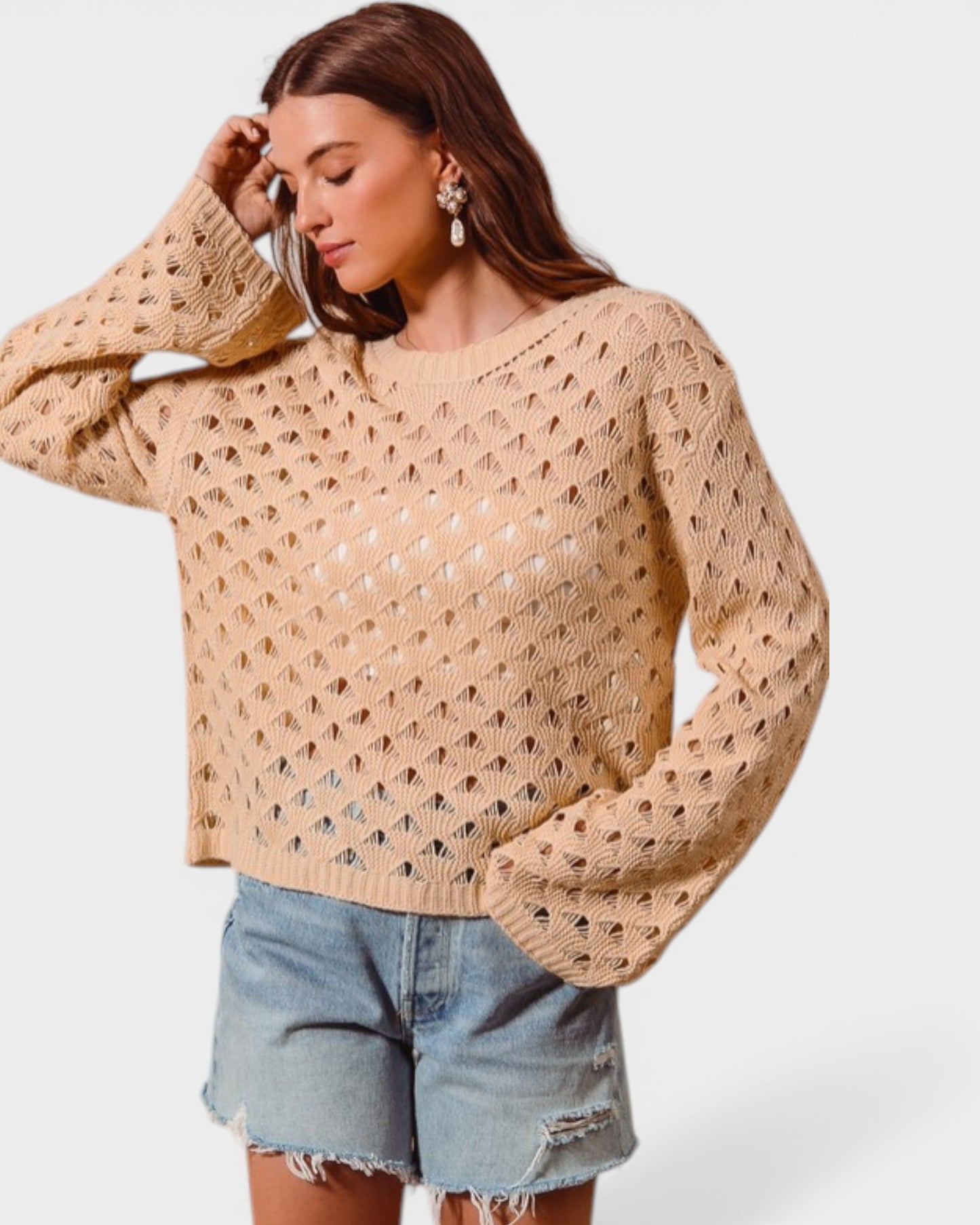 Woman wearing a beige open-knit sweater and denim shorts on a white background