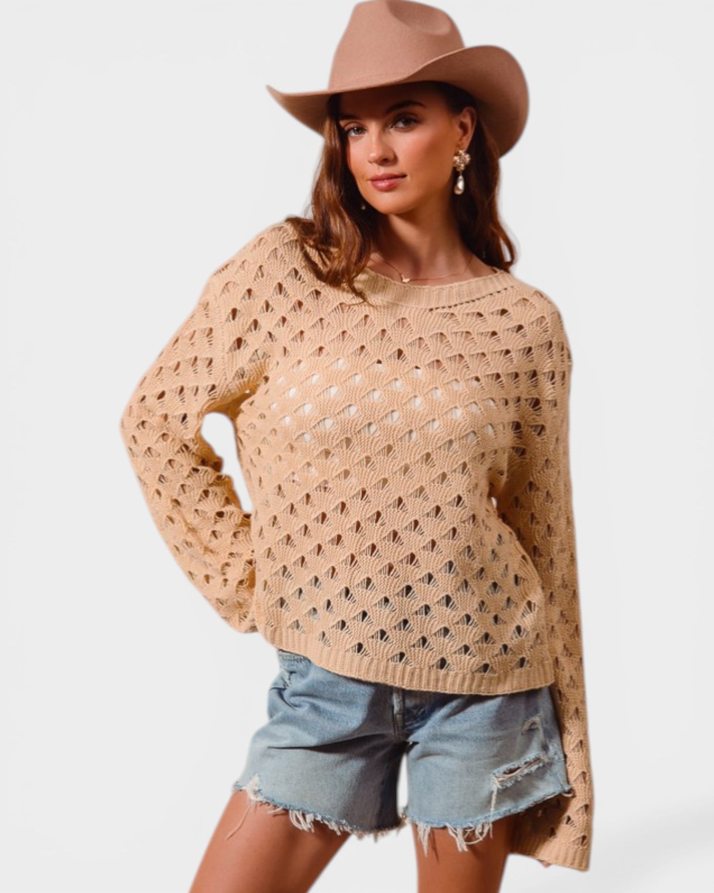 Woman wearing a beige crochet sweater, denim shorts, and a brown hat on a white background