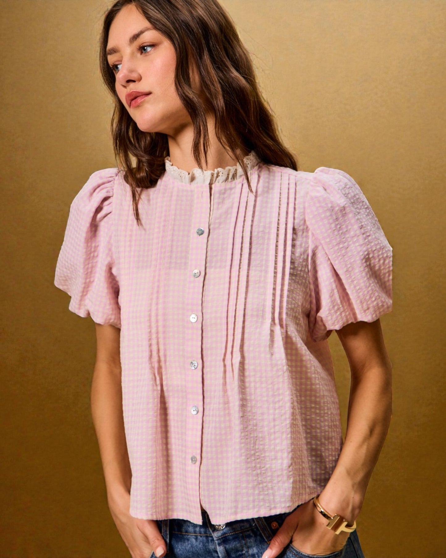 Woman wearing a pink blouse with puffed sleeves against a gold background