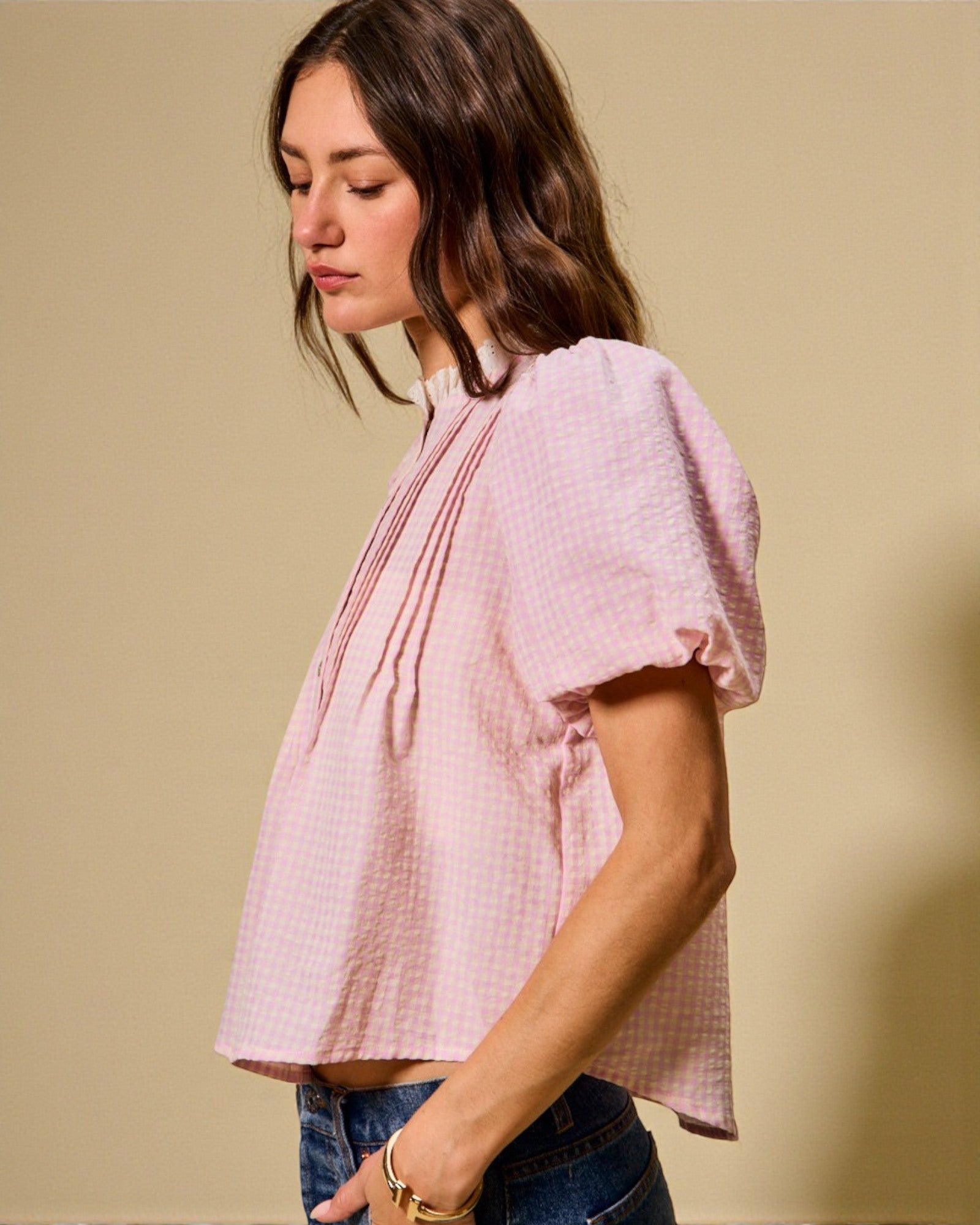Woman wearing a pink blouse with puffed sleeves against a beige background
