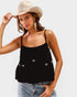 Woman wearing a black top with bow details, light blue jeans, and a beige hat on a white background