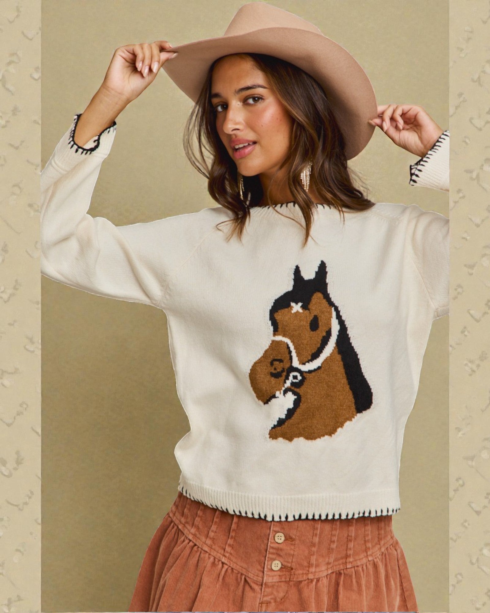 Woman wearing a sweater with a horse design and a wide-brimmed hat against a beige background