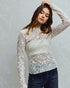 Woman wearing a white lace long-sleeve top against a light gray background