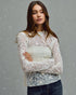 Woman wearing a white lace top with a plain background