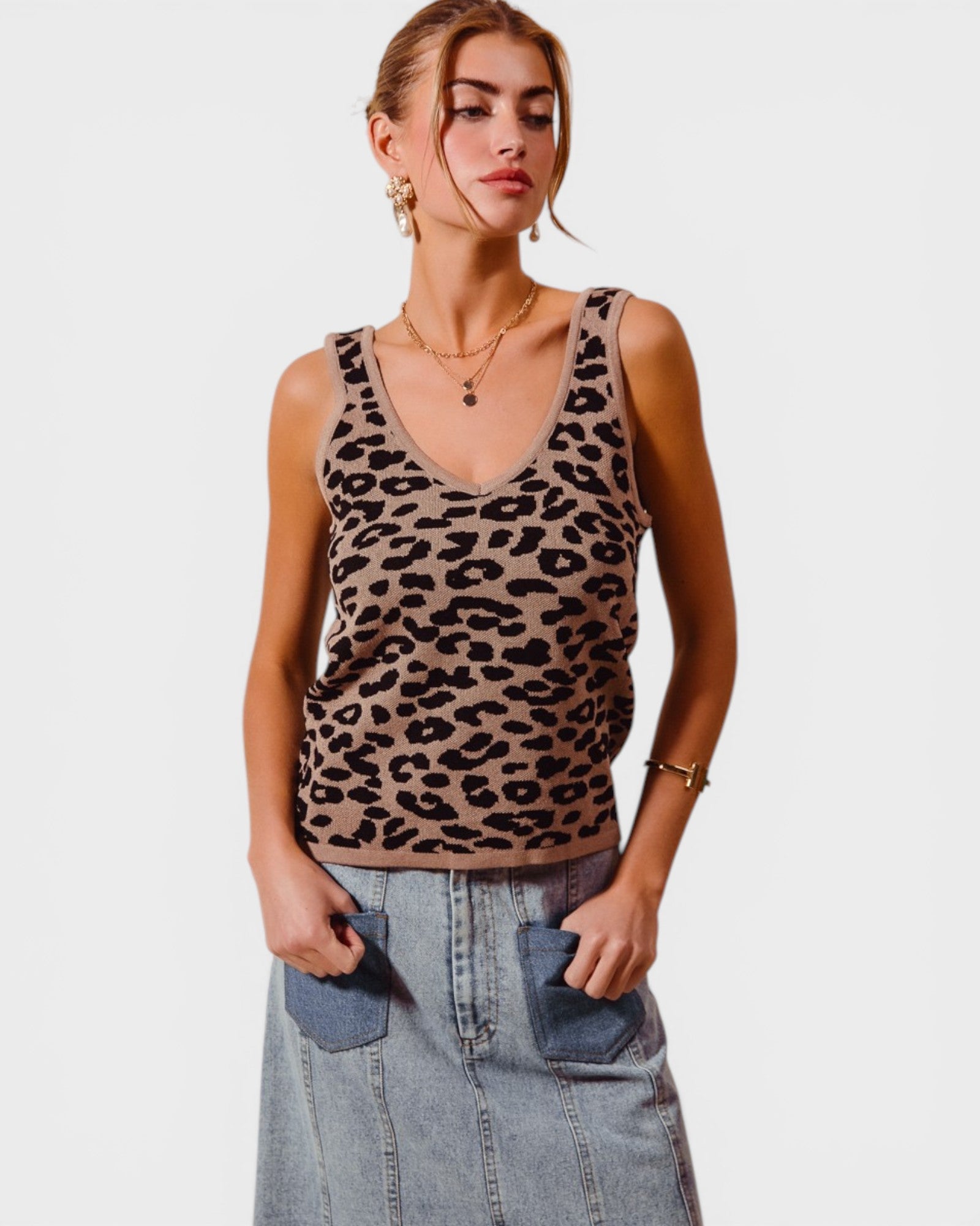 Woman wearing a leopard print tank top and denim skirt on a plain background
