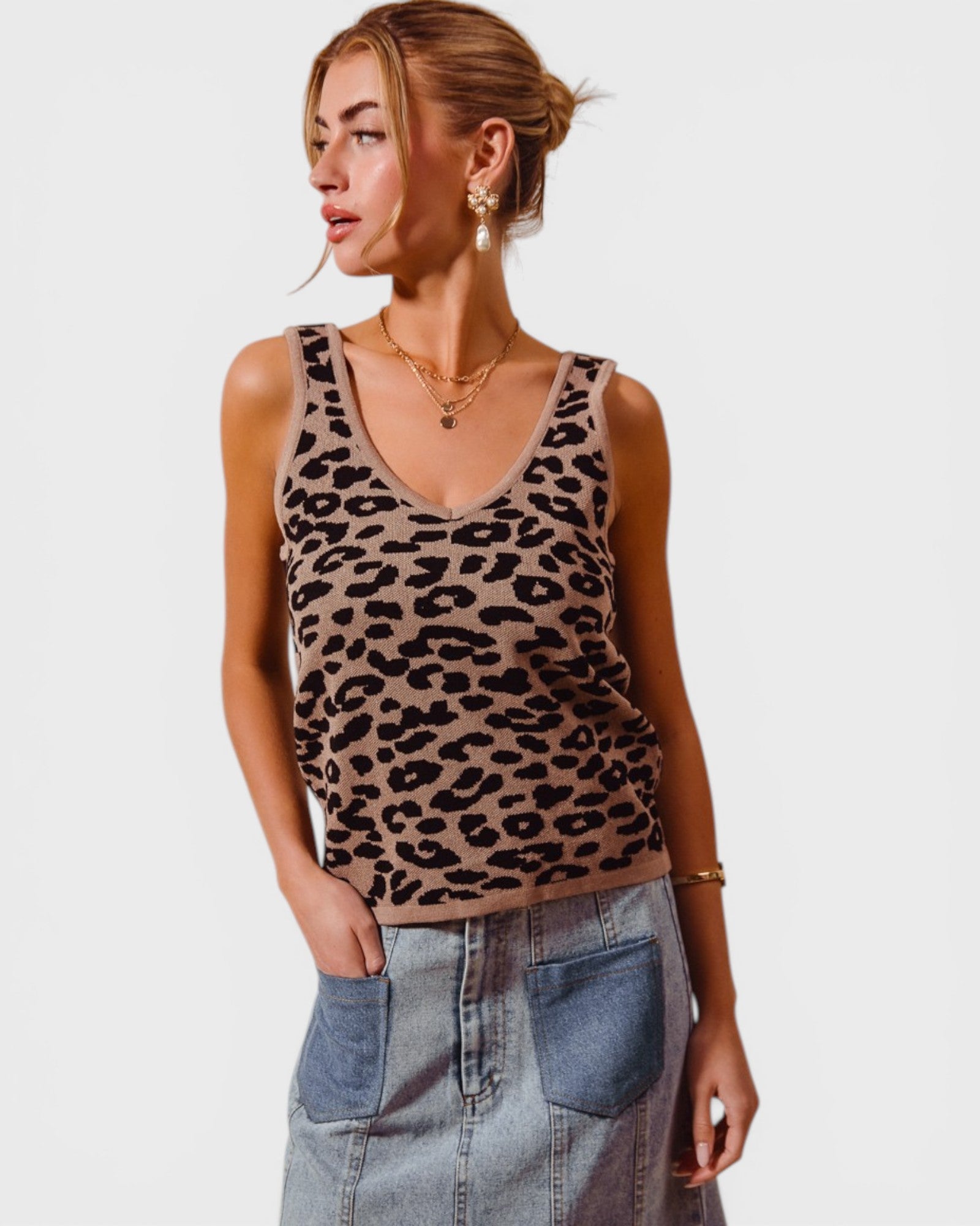 Woman wearing a leopard print tank top and denim skirt on a plain background