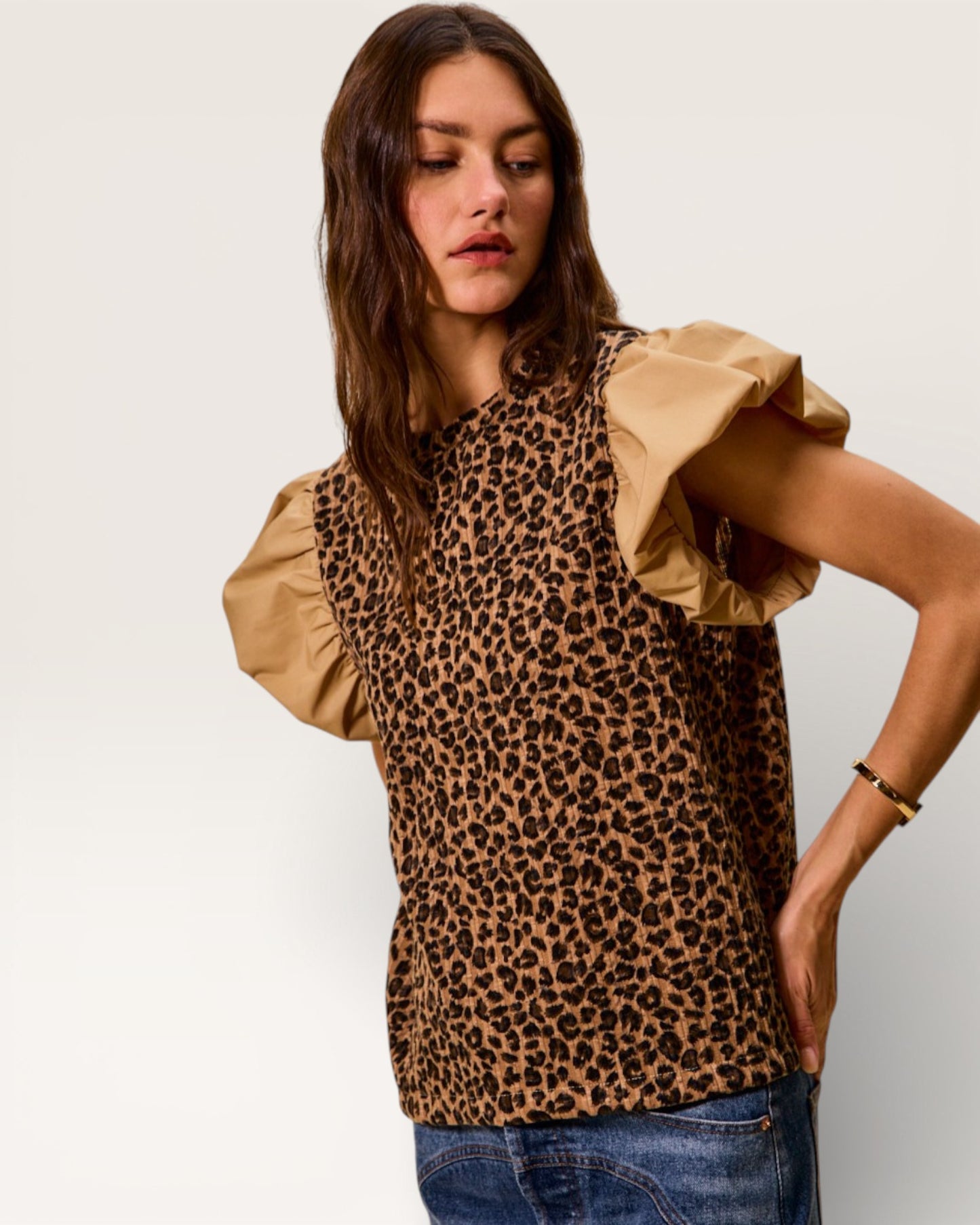 Woman wearing a leopard print top with beige sleeves against a plain background
