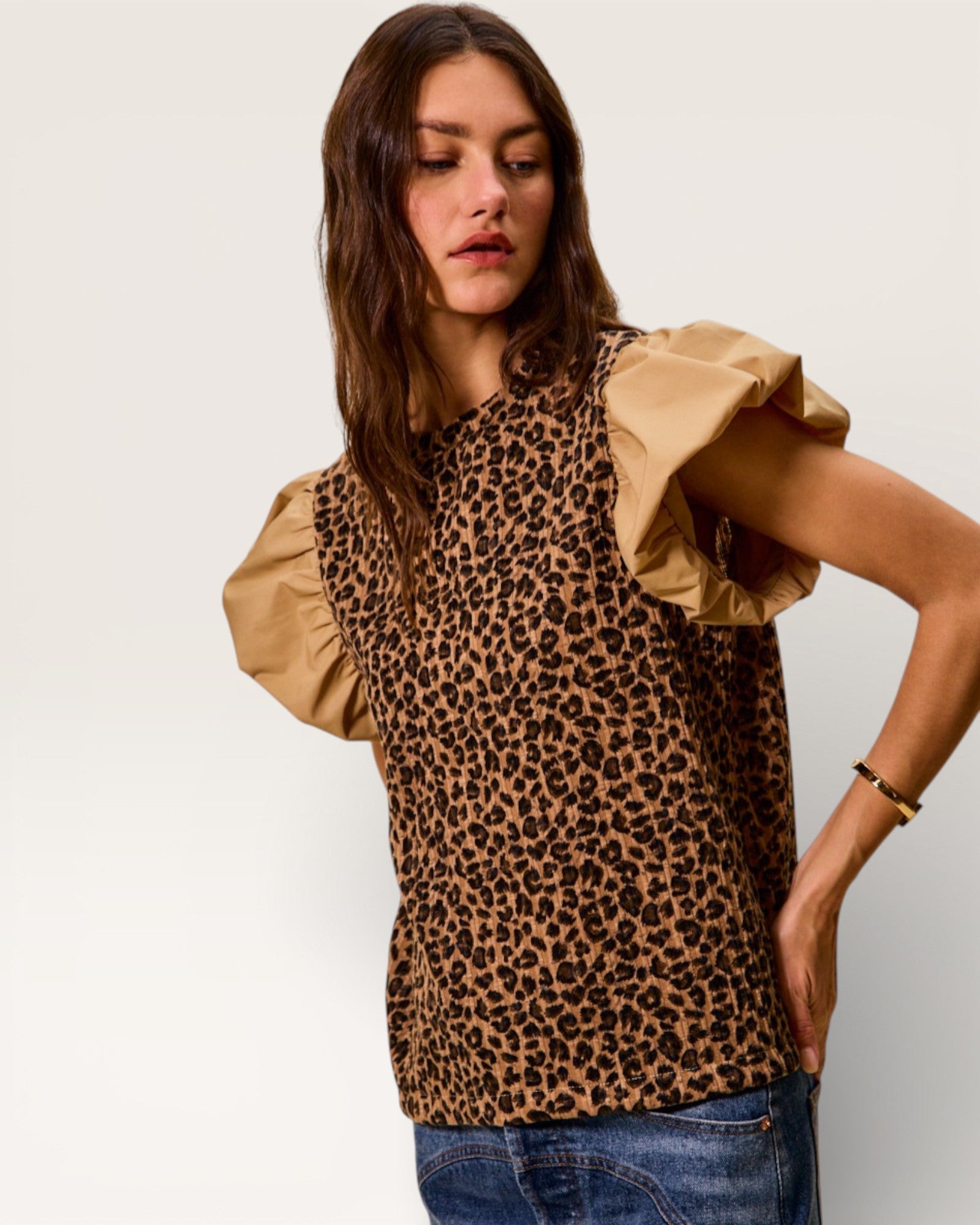 Woman wearing a leopard print top with beige sleeves against a plain background