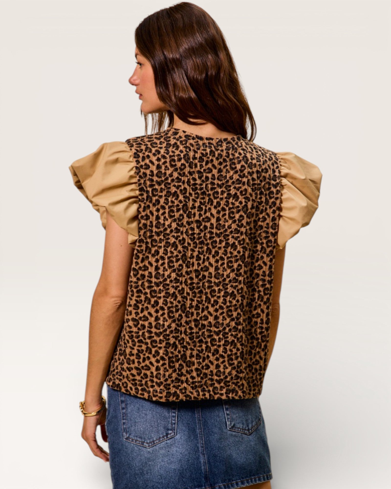 Woman wearing a leopard print top with ruffled sleeves on a plain background