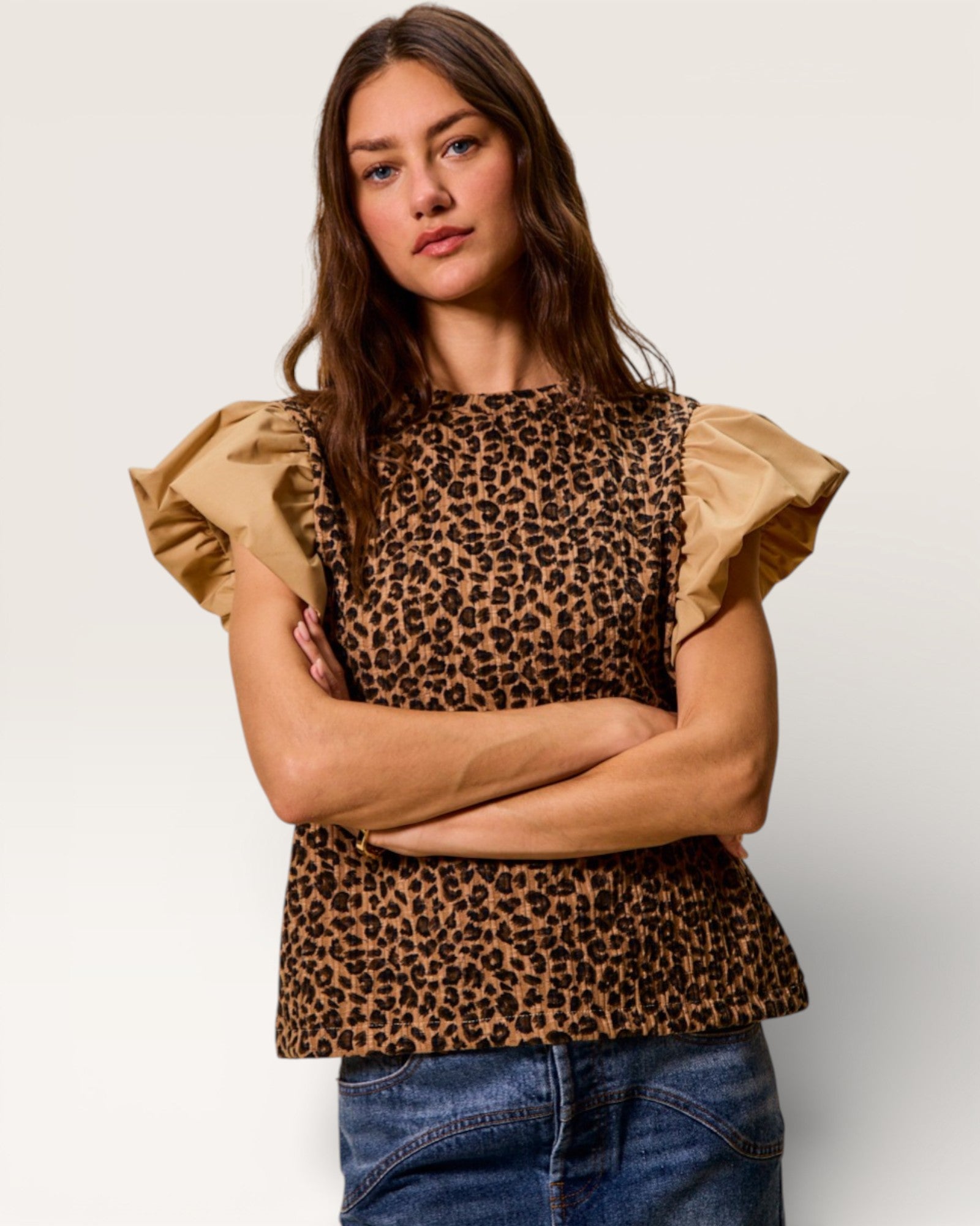 Woman wearing a leopard print top with ruffled sleeves on a plain background