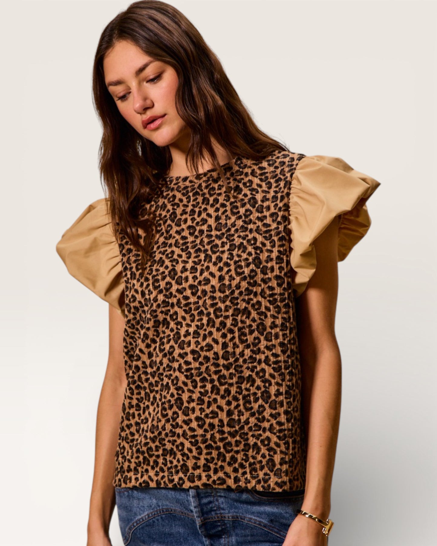 Woman wearing a leopard print top with ruffled sleeves on a plain background