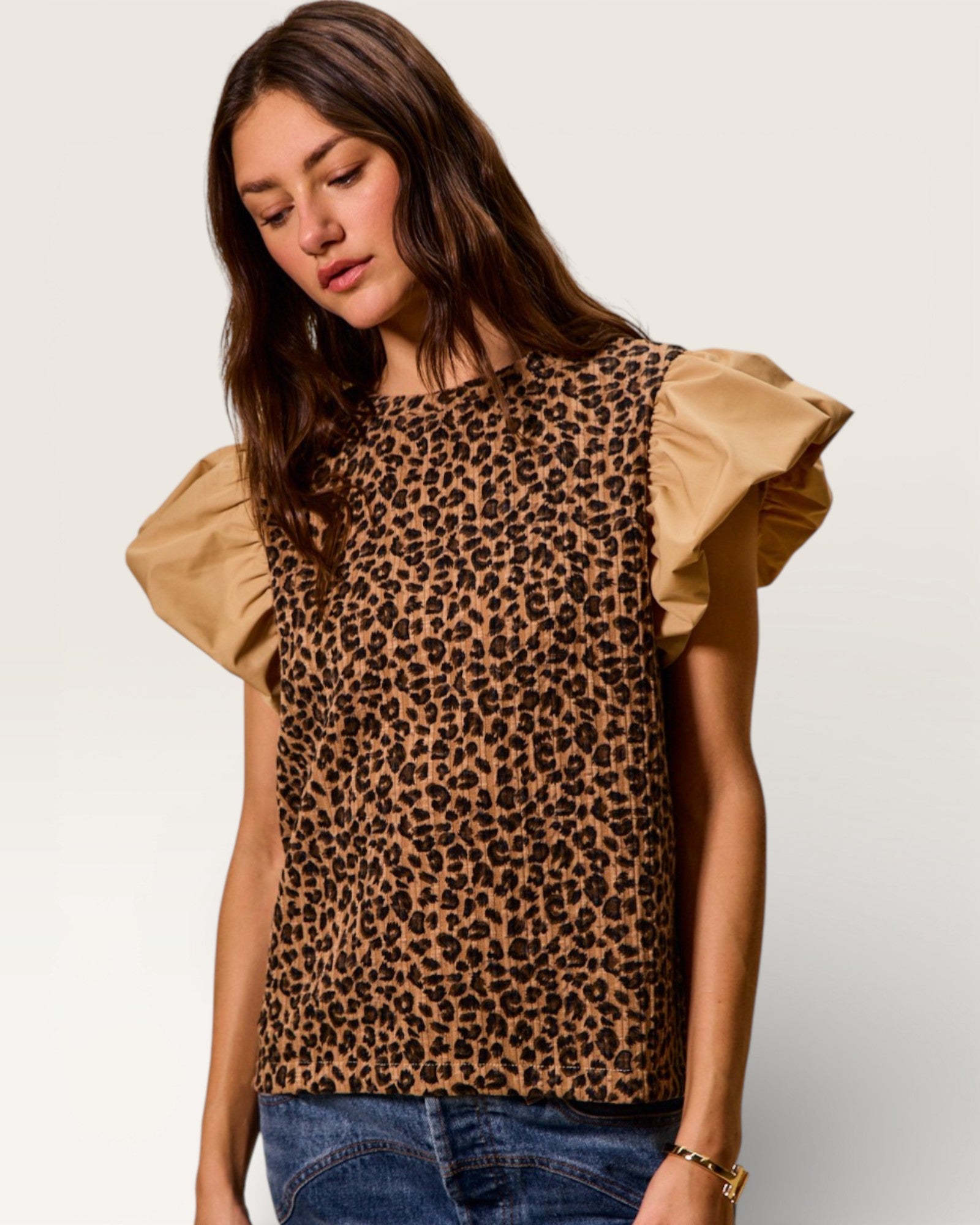 Woman wearing a leopard print top with ruffled sleeves on a plain background
