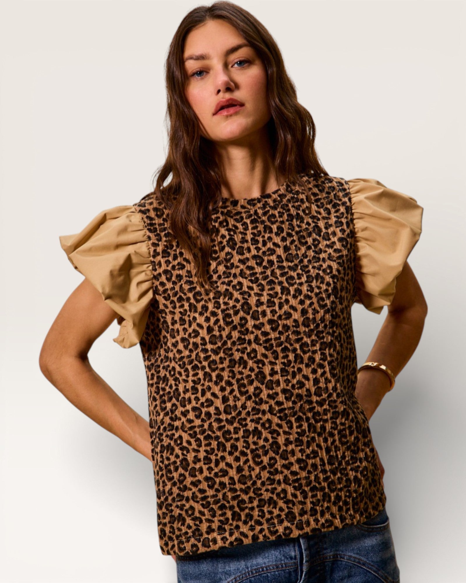 Woman wearing a leopard print top with ruffled sleeves on a plain background