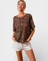 Woman wearing a leopard print top and white shorts on a plain background
