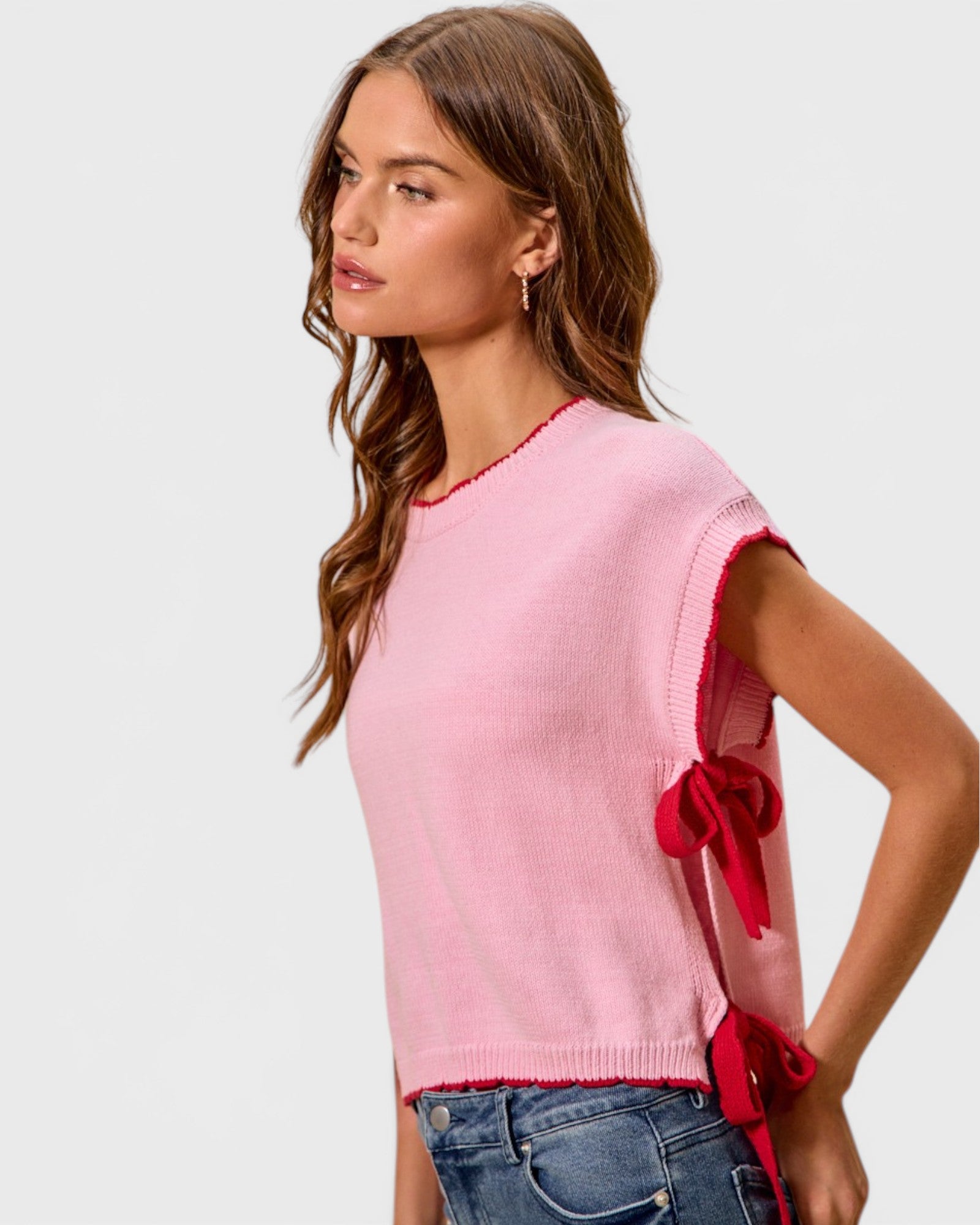 Woman wearing a pink sweater with red accents on a plain background