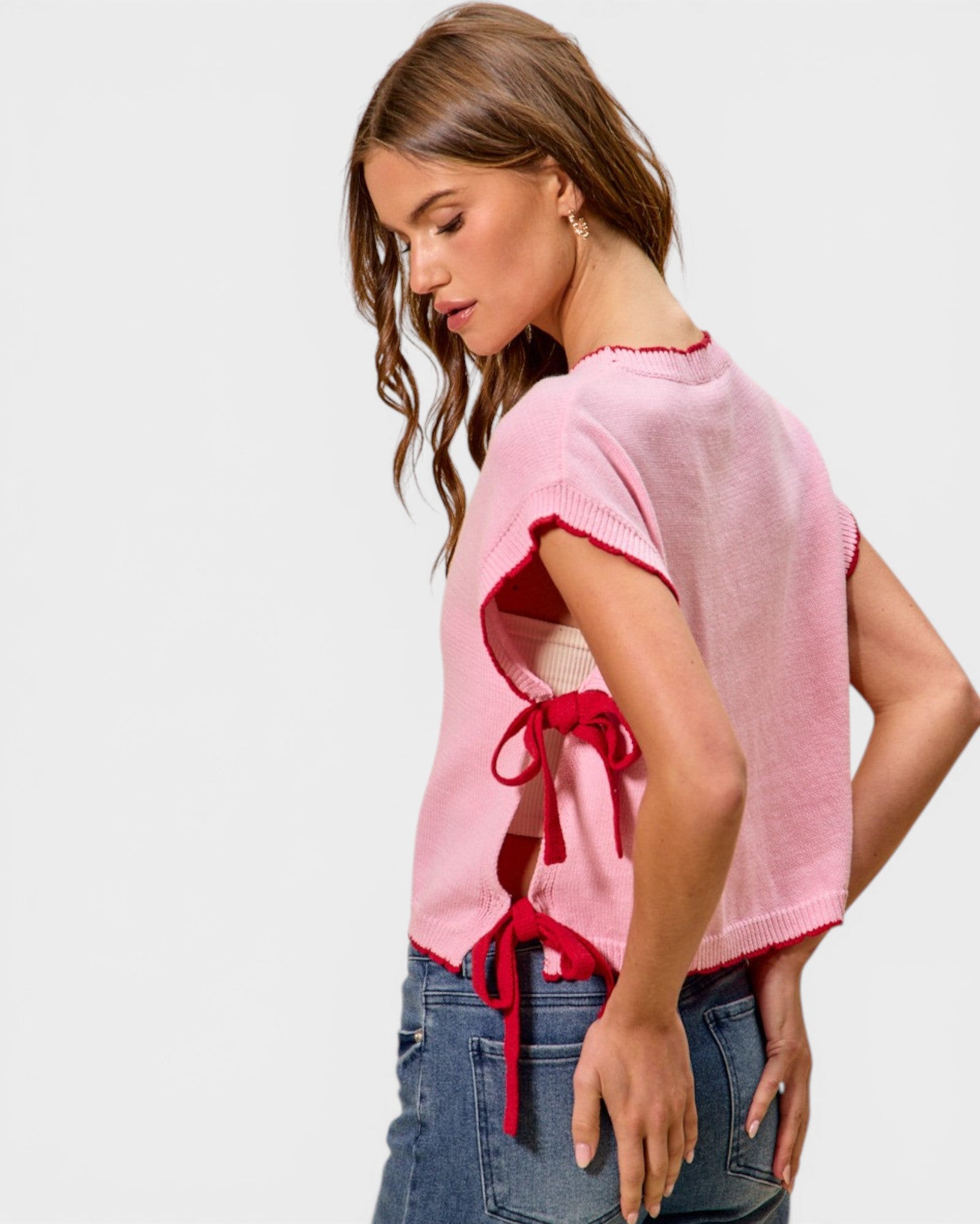 Woman wearing a pink top with ruffled sleeves and red accents, standing against a plain background.