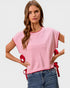 Woman wearing a pink sweater with red trim and ribbons, standing against a plain background