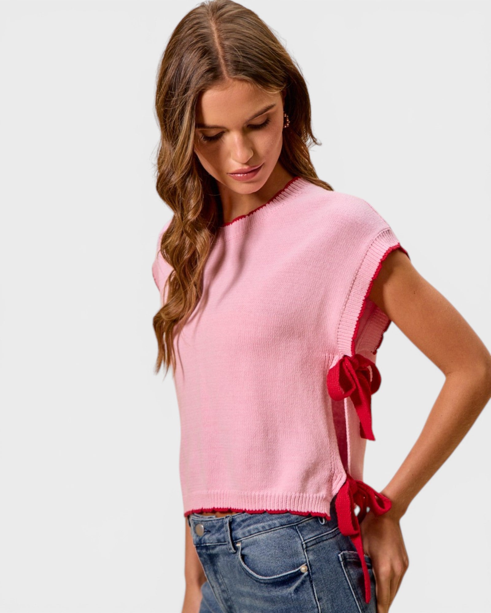 Woman wearing a pink sweater with red bow details on a white background