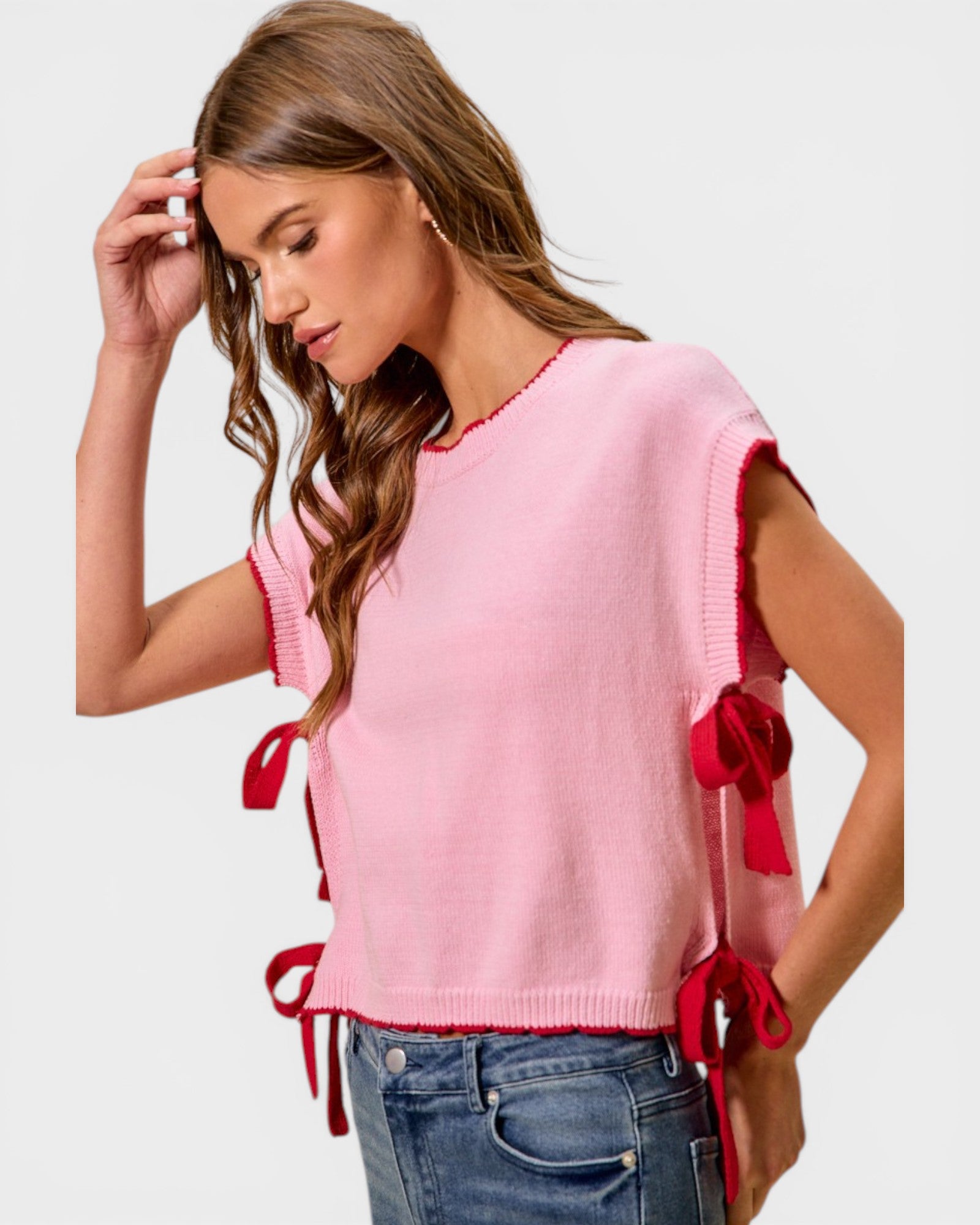 Woman wearing a pink sweater with red tie details on a plain background