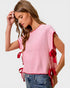 Woman wearing a pink sweater with red tie details on a plain background