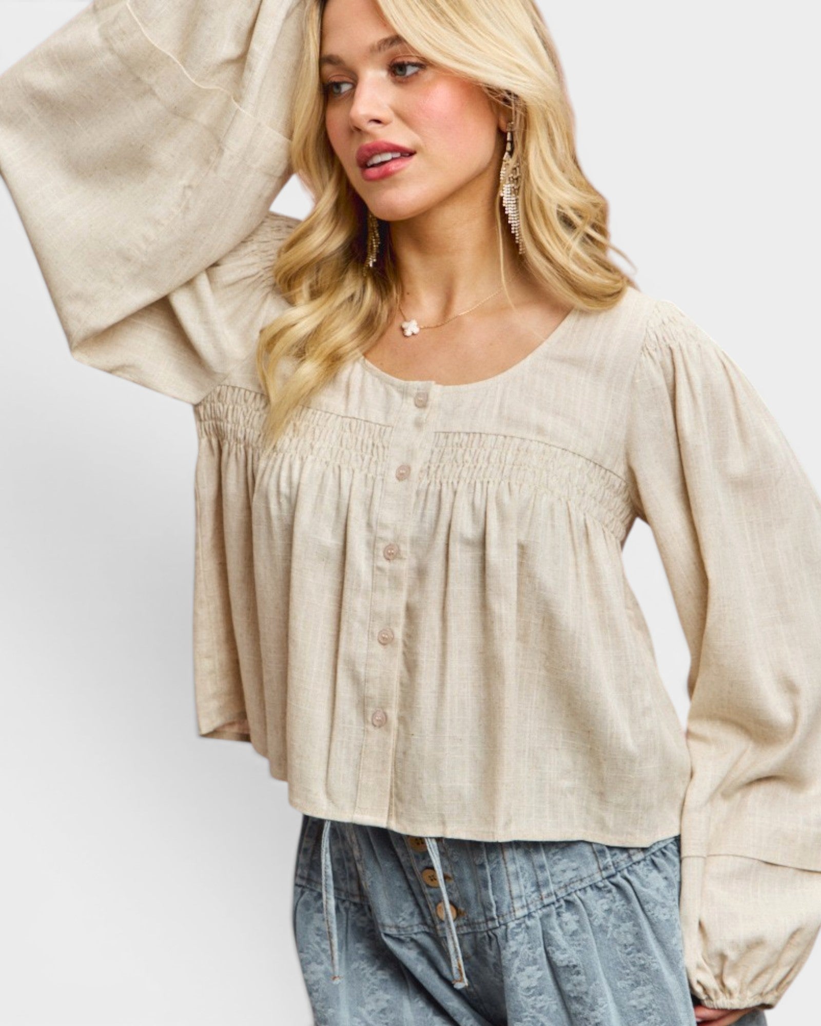 Woman wearing a beige blouse with long sleeves against a white background