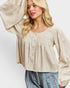 Woman wearing a beige blouse with long sleeves against a white background